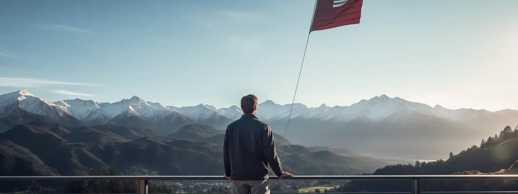 A Person Standing On A Balcony, Looking Into The Distance With A Flag Planted On A Distant Mountain Peak.